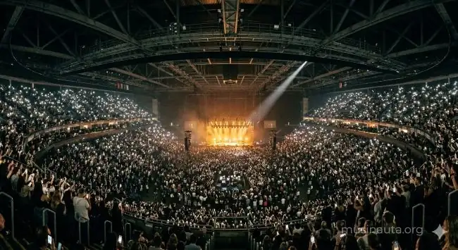 Interior de un gran estadio cubierto completamente lleno con luces de escenario doradas y público de pie