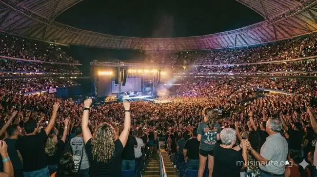 Interior de estadio cubierto completamente lleno con 67.000 personas y luces de escenario rosadas y doradas