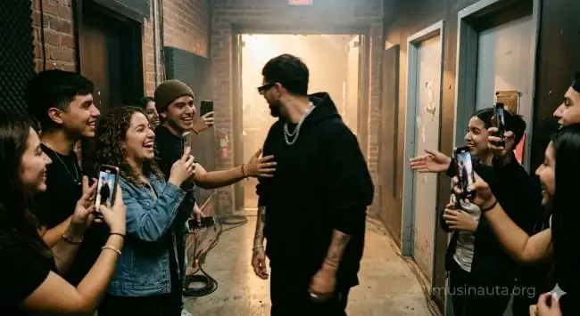 Grupo de fans latinoamericanos sonriendo y grabando con celulares mientras un artista urbano atraviesa un pasillo backstage antes de un concierto masivo nocturno