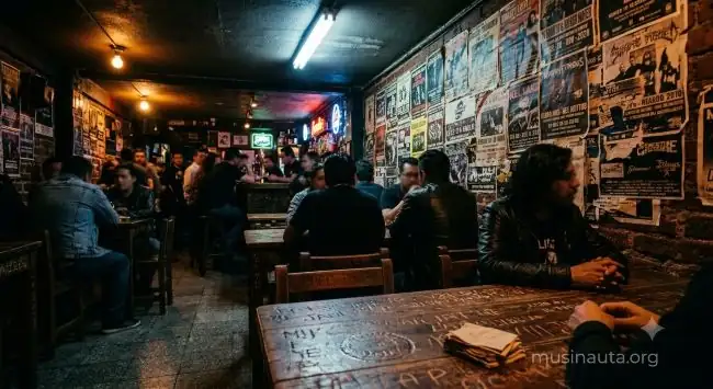 Interior de un bar de rock mexicano con mesas de madera y carteles de conciertos pegados en la pared