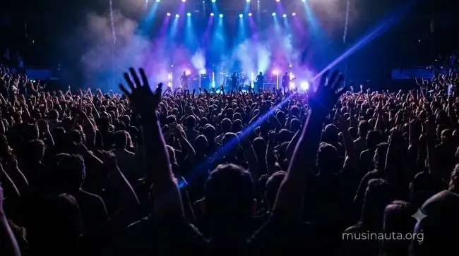 Escenario de rock visto desde el público con luces azules y siluetas de una multitud levantando los brazos