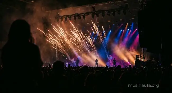 Escenario de festival con luces y pirotecnia durante un show de música urbana latina