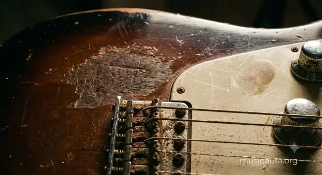 Detalle de una guitarra eléctrica con cuerdas oxidadas y cuerpo de madera rayado