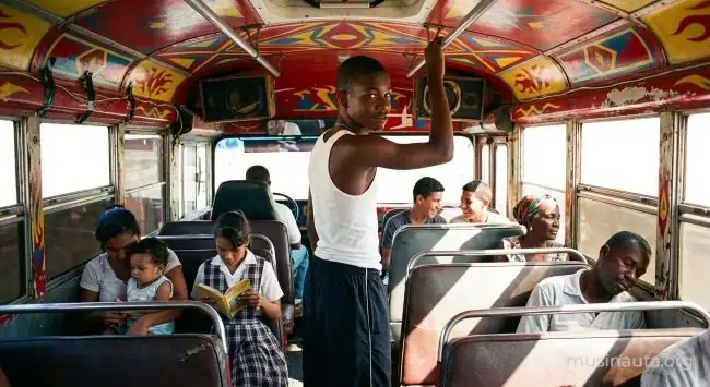 Interior de un bus urbano panameño pintado de colores intensos con pasajeros sentados y un joven de pie mirando a cámara junto a los parlantes de la cabina